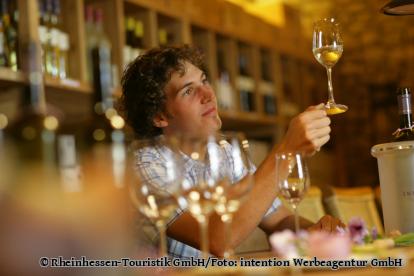 Ein Winzer hät ein Glas mit Wein gegen das Licht, um die Farbe des Weins zu prüfen. - Foto von Rheinhessen-Touristik GmbH/Foto: intention Werbeagentur GmbH
