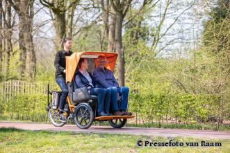 Ein Paar wird von einem jungen Mann auf einer E-Rikscha durch einen Park gefahren - Foto von Pressefoto van Raam