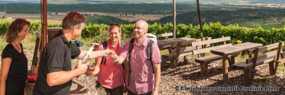 Winzer des Weinausschanks füllen über den Tisch hinweg die Gläser eines Wandererpärchens - Foto von Rheinhessen-Touristik Dominik Kretz