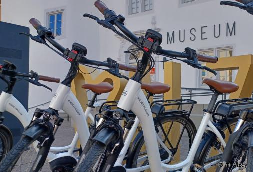 Ein Paar mit zwei E-Bikes vor der Tourist Information. Beide lächeln sich zu. - Foto von © TI Alzey
